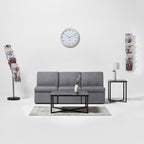 Gray sofa in a living room with a clock on the wall and magazine holders.