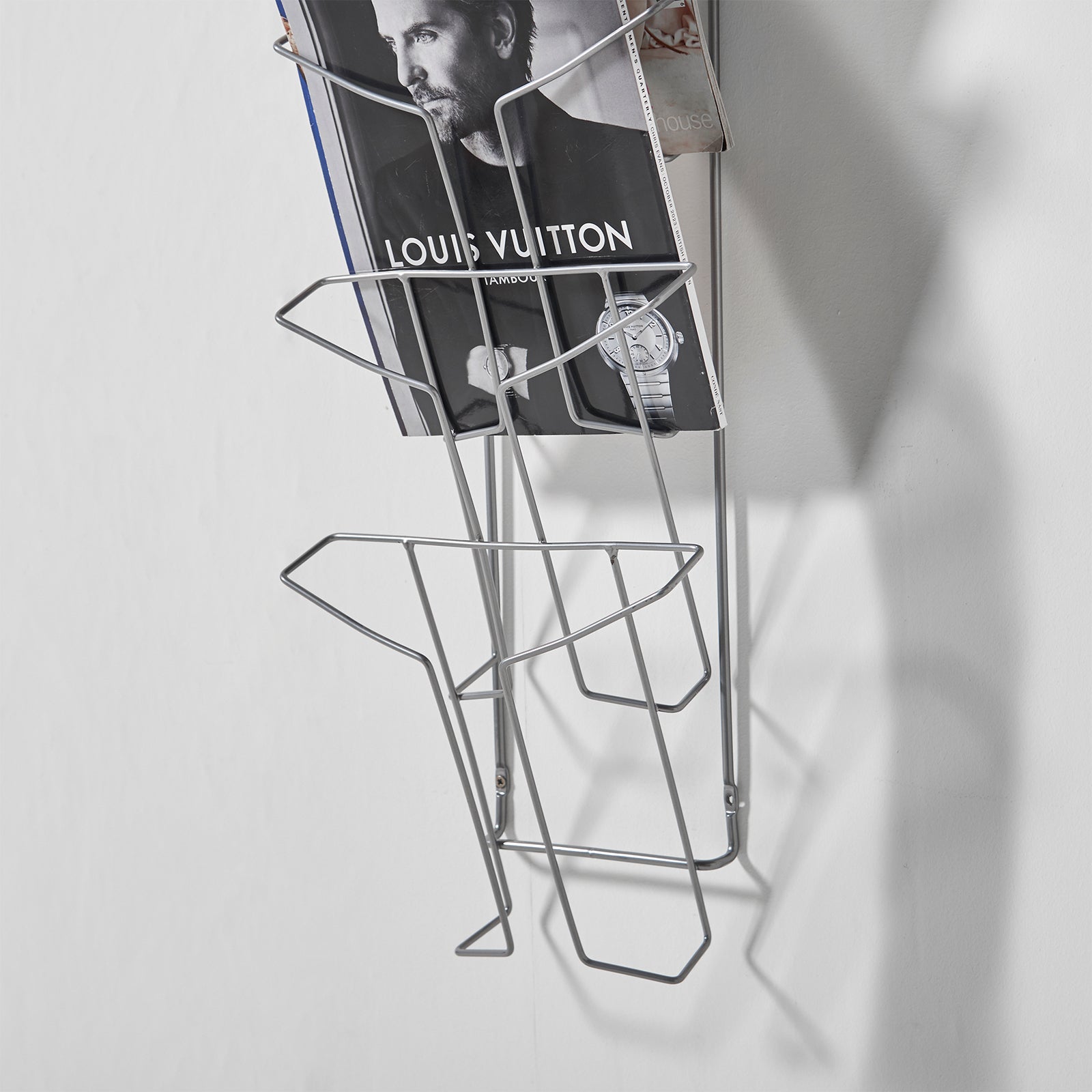 Metal wire wall display with a magazine on a grey background