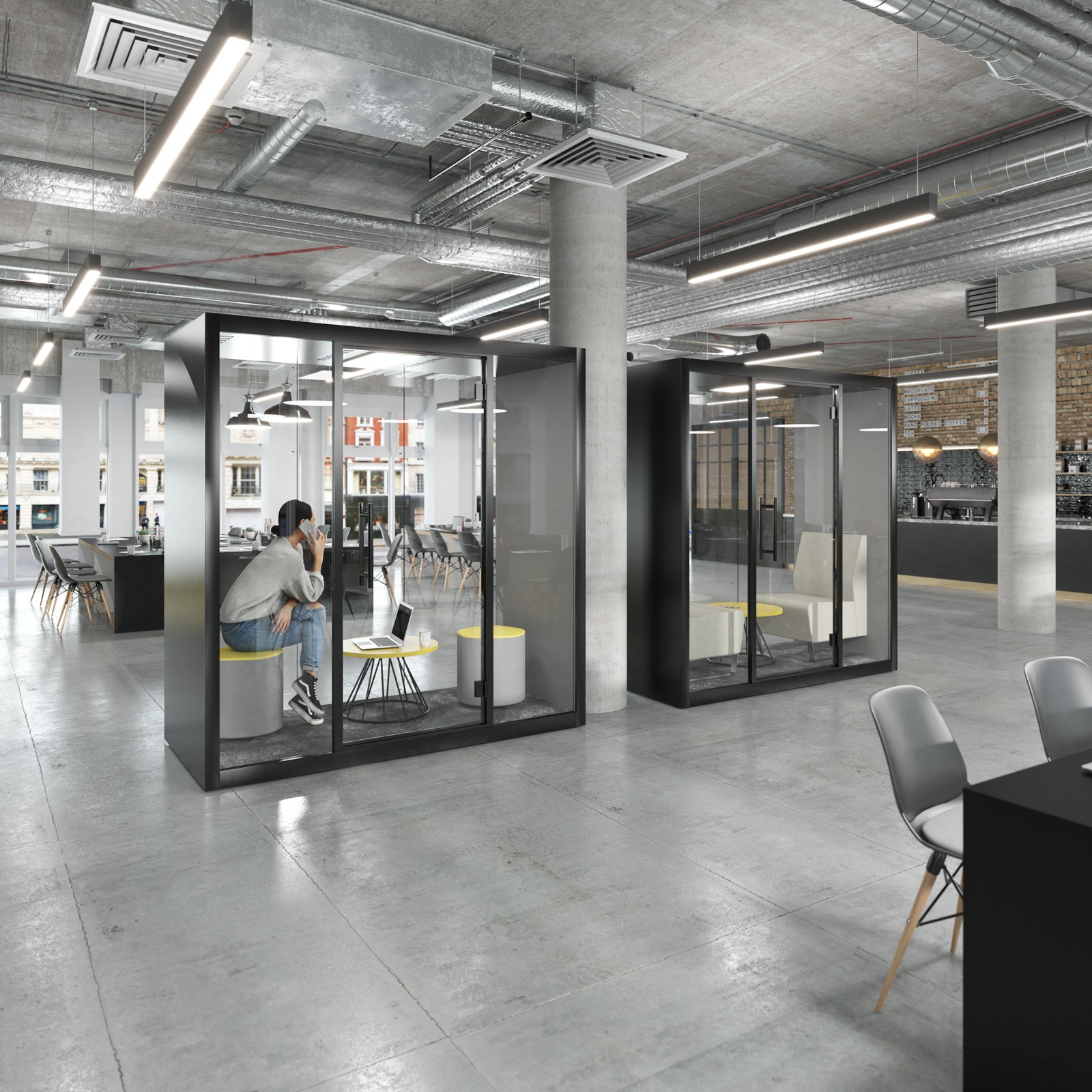 Modern office interior with two black glass privacy callout booths. One booth is occupied by a person sitting on a gray chair, while the other stands empty.