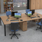 Modern office setup with desks, chairs, and computer monitors in a room with bookshelves and large windows.