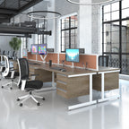 Modern office desk setup with dual wood-grain desktops, white metal frames, and orange-tinted dividers, shown in a bright office environment with office chairs and computer monitors.