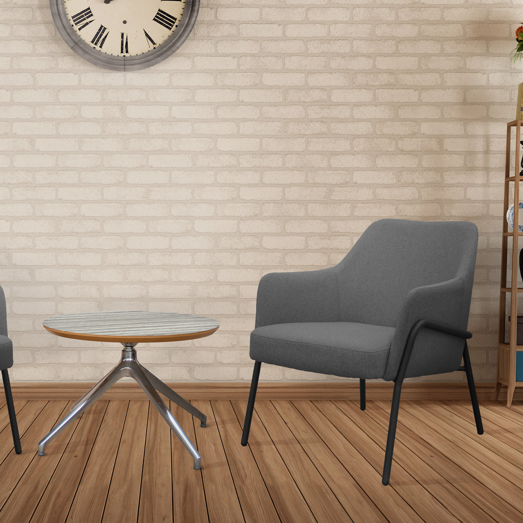 Grey armchair and small round table in a room with wooden flooring and brick wall.
