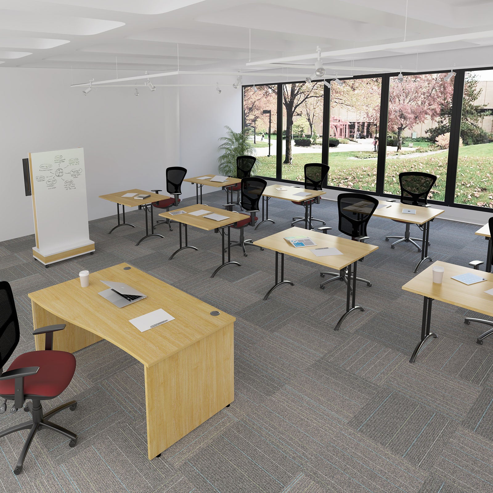 A modern classroom or office space with multiple light wood desks, black mesh office chairs, a whiteboard, and large windows overlooking a landscaped outdoor area.