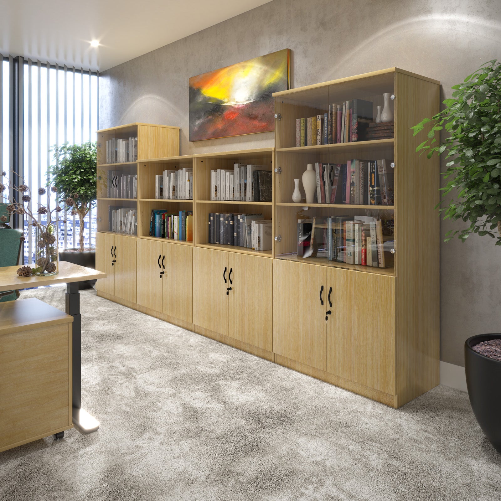 A long modular light wood office bookcase and storage cabinet unit with open shelves and closed doors, shown in a modern office interior with books, vases, plants, and a wall painting.