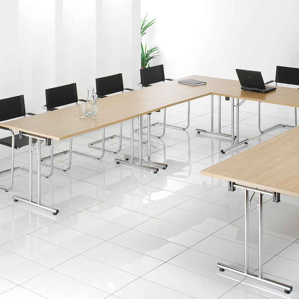 Modern office setup with long wooden tables and black chairs in a bright room.