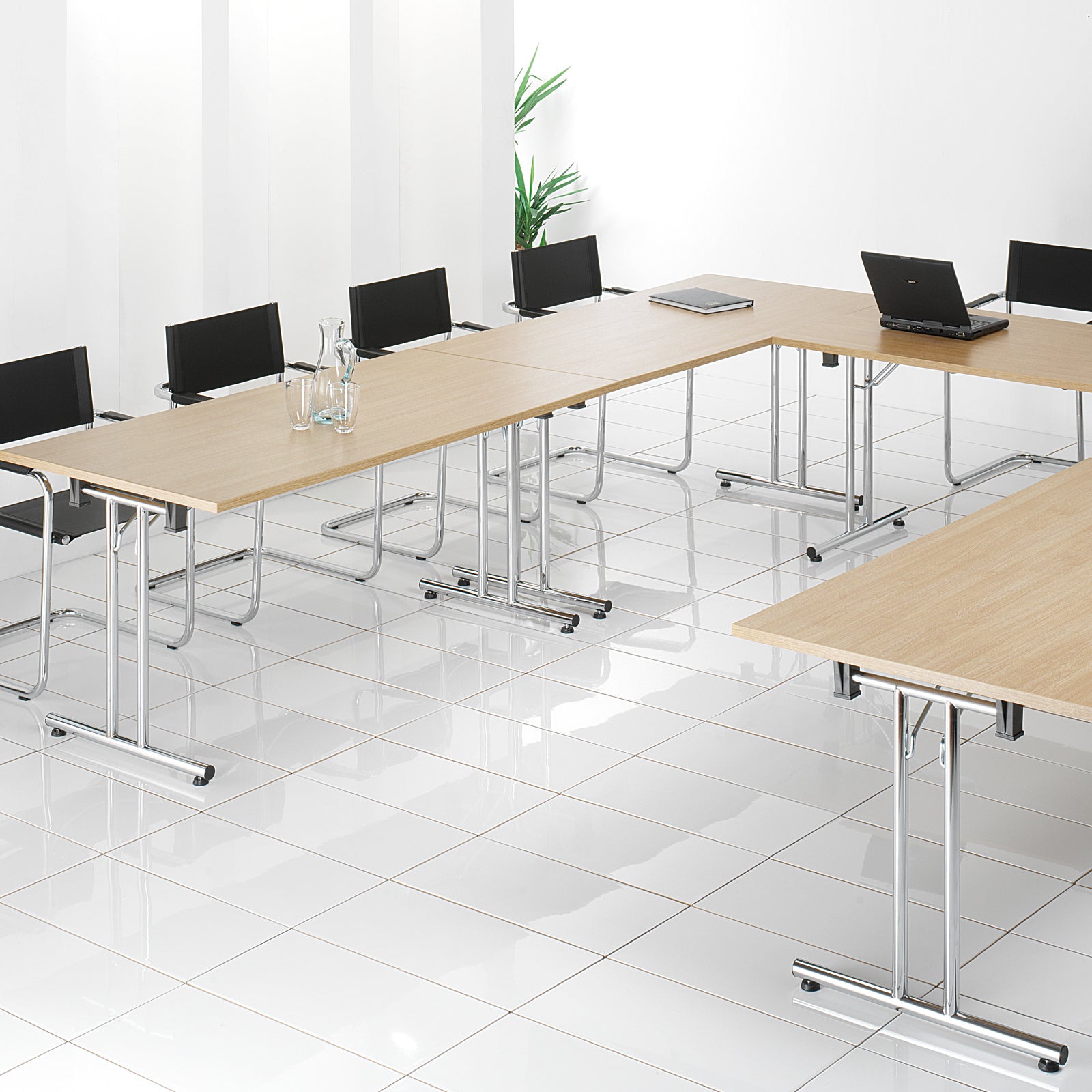 Modern office setup with long wooden tables and black chairs in a bright room.