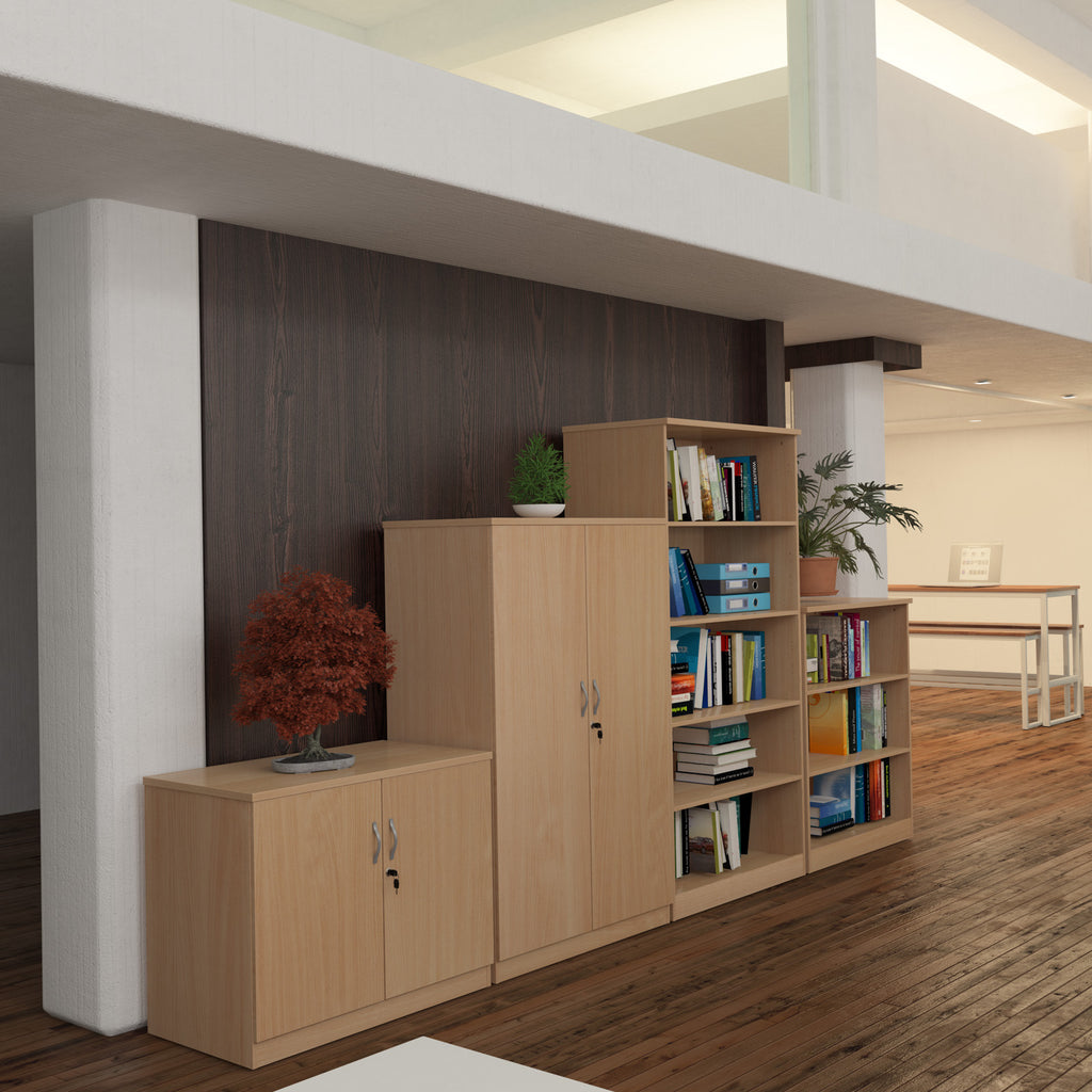 A light wood office furniture set consisting of a low cabinet, a tall double-door cabinet, and a shelving unit with books and plants, shown in a modern office interior.