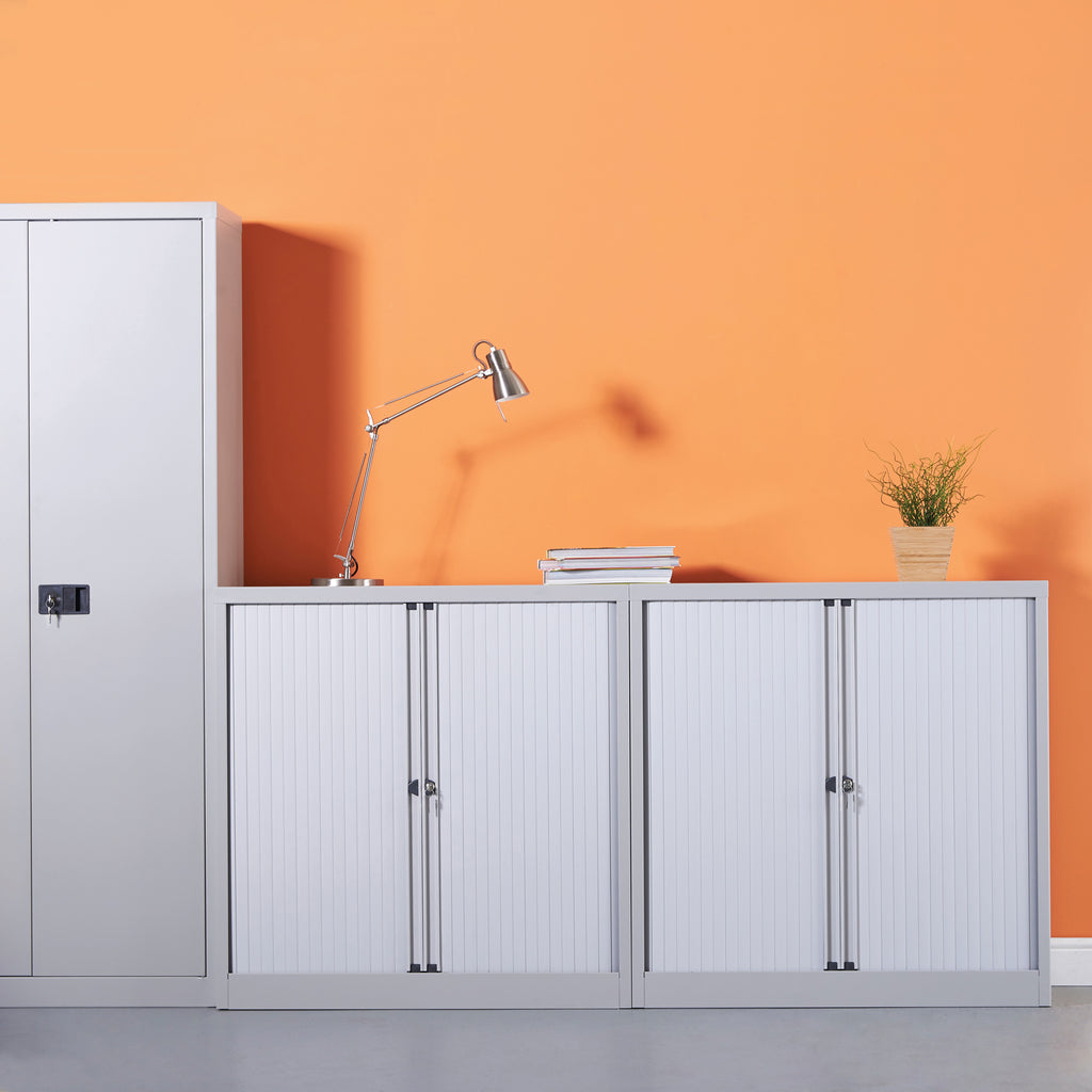 Light grey cabinets against an orange wall with a lamp and plant.