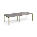 Four back-to-back desks with grey wood-effect tops and green metal frame on a white background