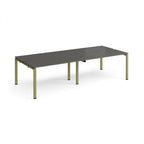 Four back-to-back desks with grey tops and green metal frame on a white background