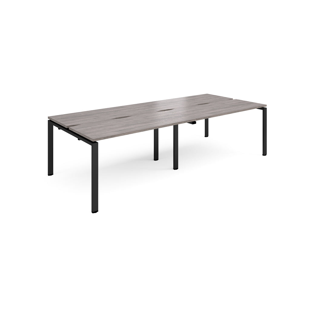 Four back-to-back desks with grey wood-effect tops and black metal frame on a white background