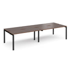 Four back-to-back desks with wood-effect tops and black metal frame on a white background