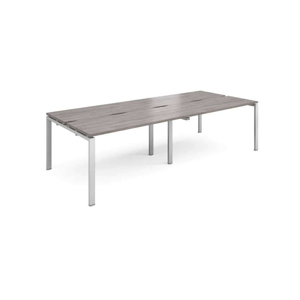 Four back-to-back desks with grey wood-effect tops and silver metal frame on a white background