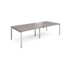 Four back-to-back desks with grey wood-effect tops and silver metal frame on a white background