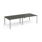 Four back-to-back desks with grey tops and silver metal frame on a white background
