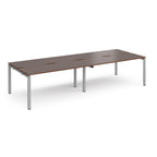 Four back-to-back desks with wood-effect tops and silver metal frame on a white background