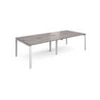 Four back-to-back desks with grey wood-effect tops and white metal frame on a white background
