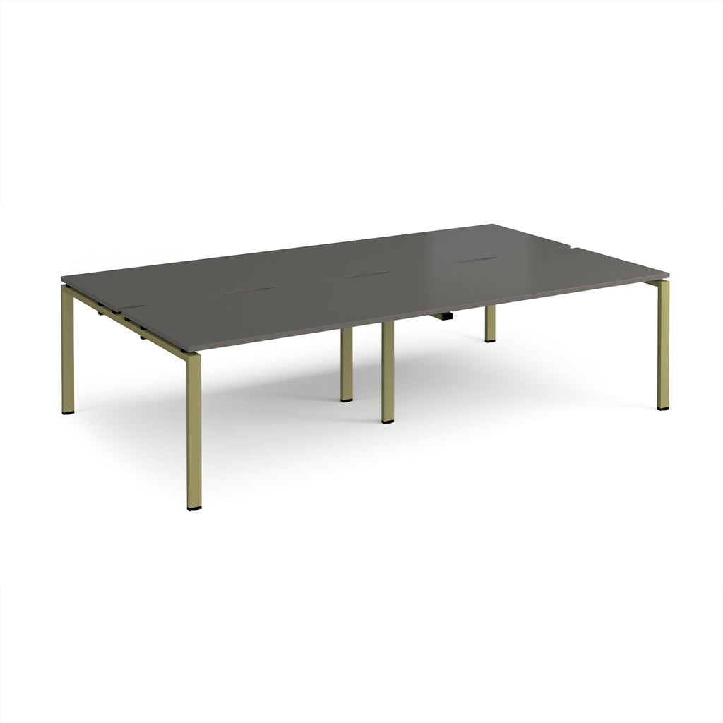 Four back-to-back desks with grey tops and green metal frame on a white background