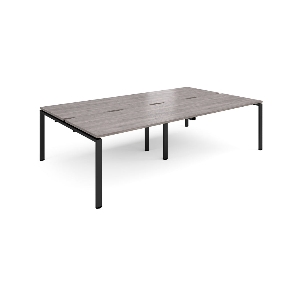 Four back-to-back desks with grey wood-effect tops and black metal frame on a white background