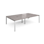 Four back-to-back desks with grey wood-effect tops and silver metal frame on a white background