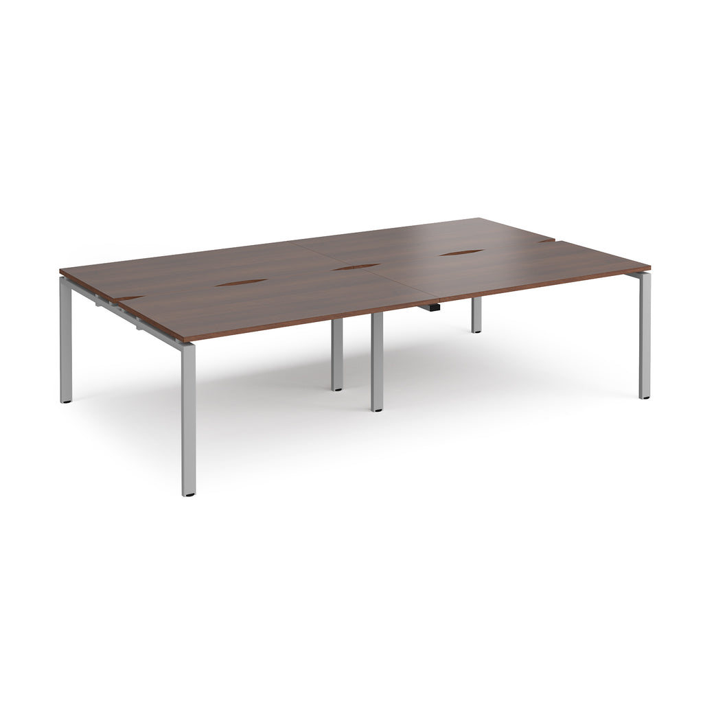 Four back-to-back desks with wood-effect tops and silver metal frame on a white background