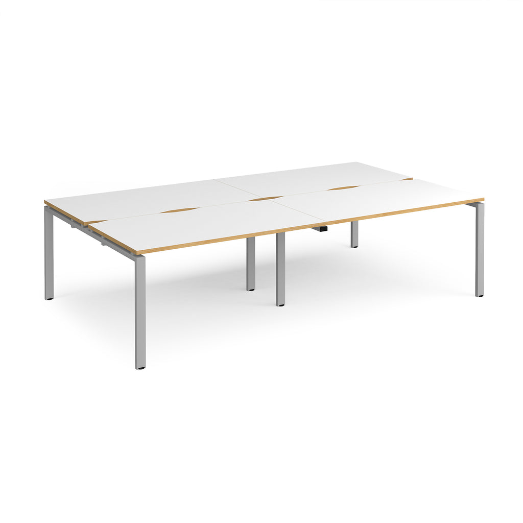 Four back-to-back desks with white tops with wooden edges and silver metal frame on a white background