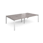 Four back-to-back desks with grey wood-effect tops and white metal frame on a white background