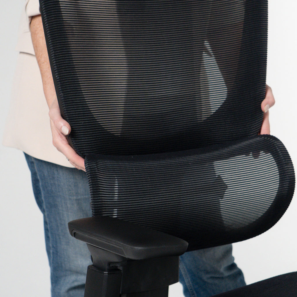 Person holding a black office chair with mesh backrest against a plain background