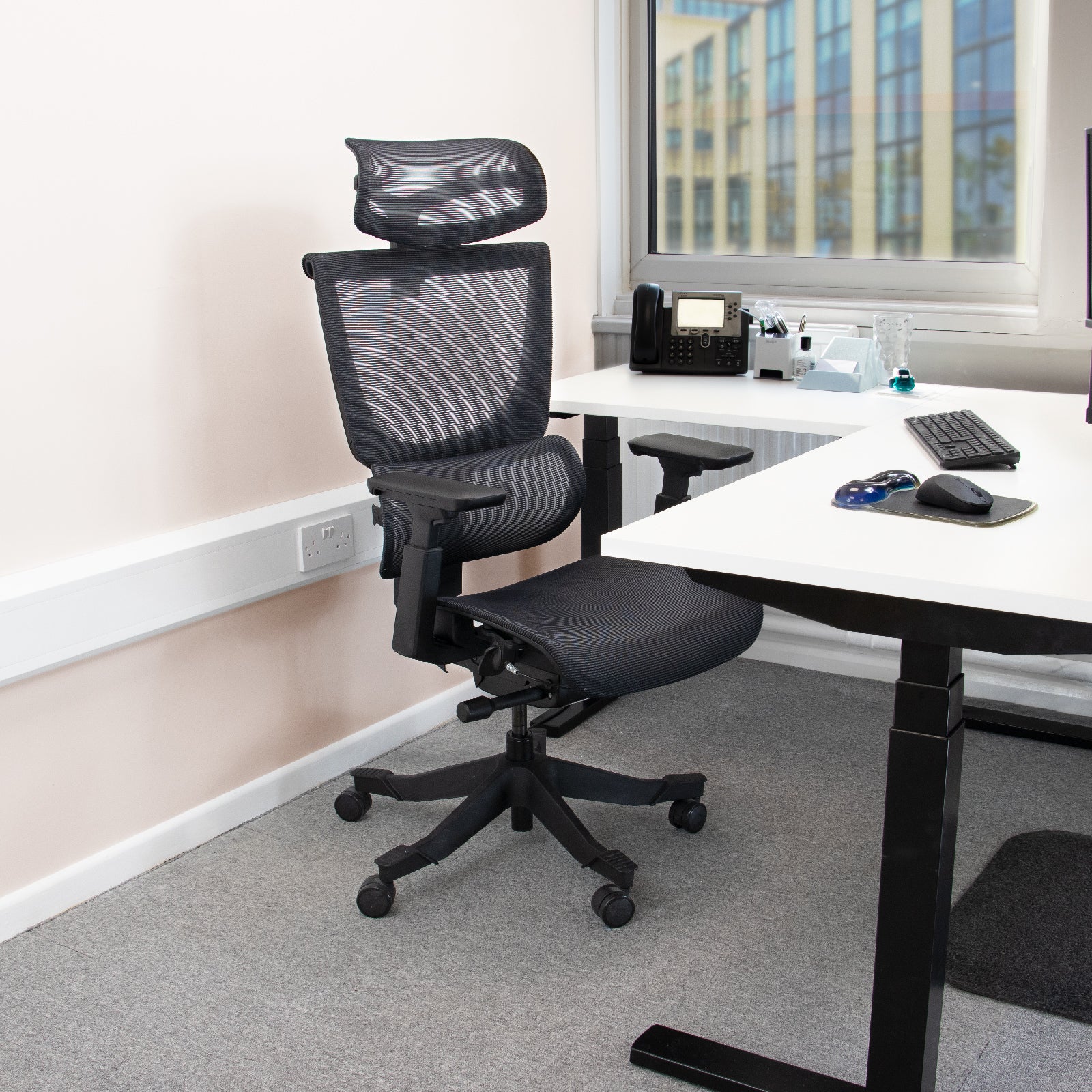 Black ergonomic chair in an office setting with a desk and window in the background.