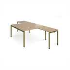 L-shaped back-to-back desks with wood-effect top and a green metal frame on a white background
