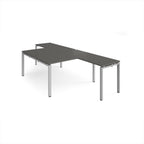 L-shaped back-to-back desks with grey top and a silver metal frame on a white background