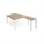 L-shaped back-to-back desks with wood-effect top and a white metal frame on a white background