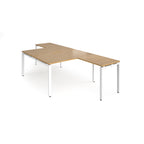L-shaped back-to-back desks with wood-effect top and a white metal frame on a white background