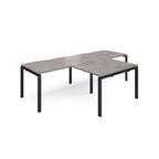L-shaped back-to-back desks with grey wood-effect top and black metal legs on a white background