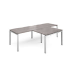 L-shaped back-to-back desks with grey wood-effect top and silver metal legs on a white background