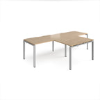 L-shaped back-to-back desks with wood-effect top and silver metal legs on a white background