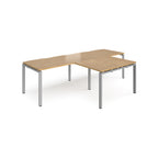 L-shaped back-to-back desks with wood-effect top and silver metal legs on a white background