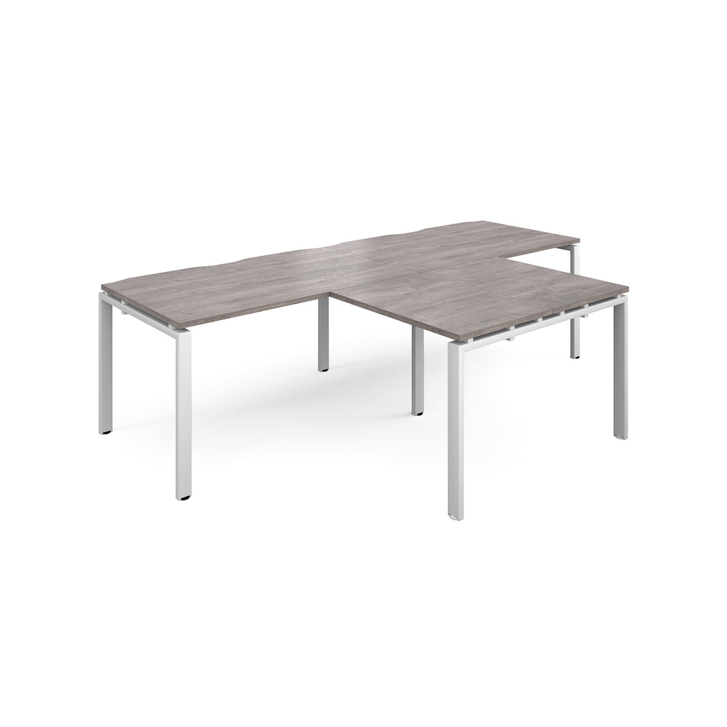L-shaped back-to-back desks with grey wood-effect top and white metal legs on a white background