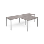 L-shaped back-to-back desks with grey wood-effect top and white metal legs on a white background