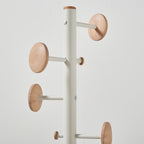 A modern coat rack with a matte white cylindrical pole and light wood grain circular hooks, shown against a plain light grey background.
