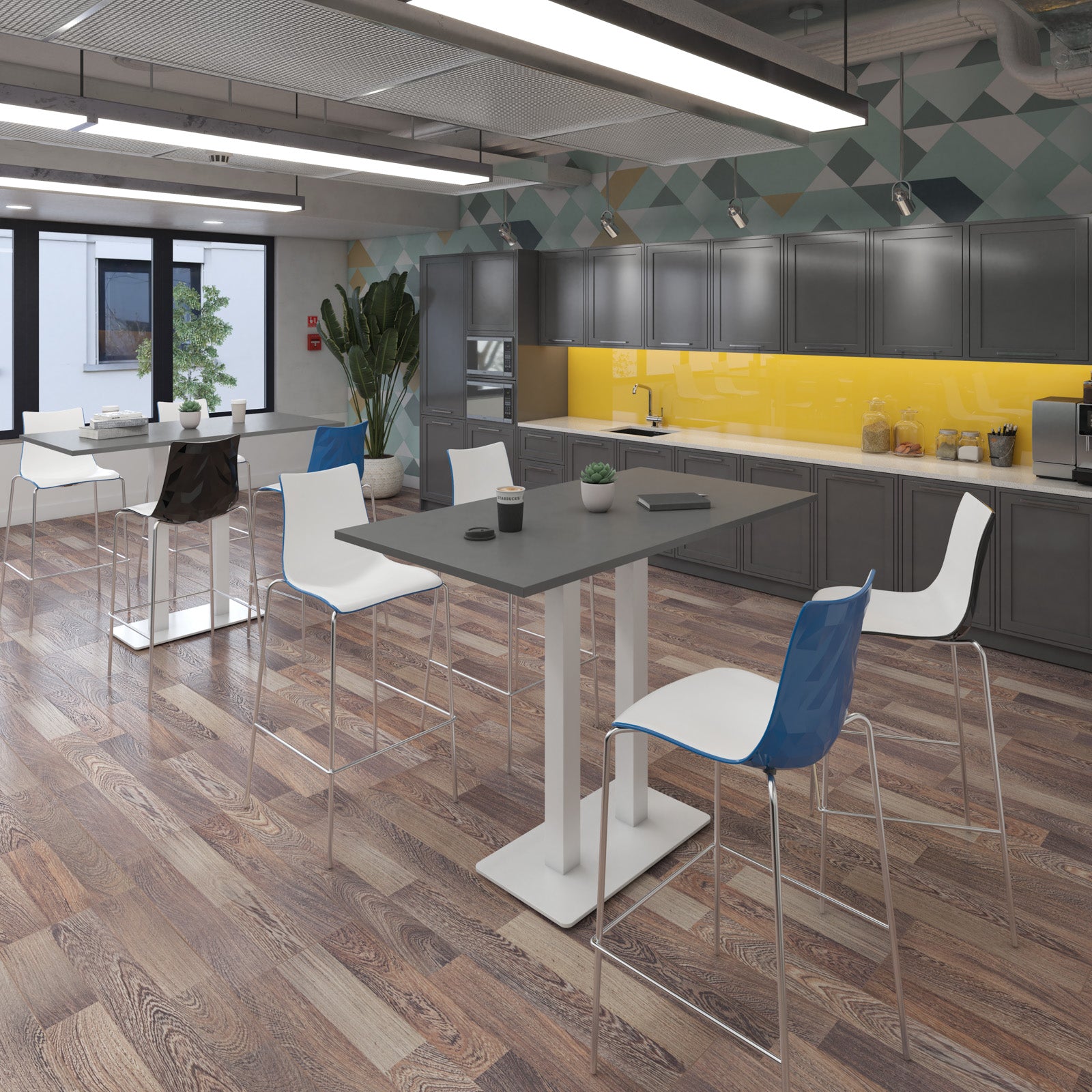 A modern office interior with a central high-top table and several bar stools, including one blue-and-white chair in the foreground. The space has wood flooring, grey cabinetry, a bright yellow backsplash, and geometric wall panels.