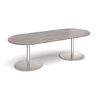 A modern oval conference table with a grey wood-grain top and dual silver metal pedestal bases, shown on a clean white background.
