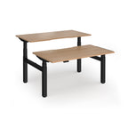 Two back-to-back height adjustable desks with shared black metal frame and wood-effect tops on a white background