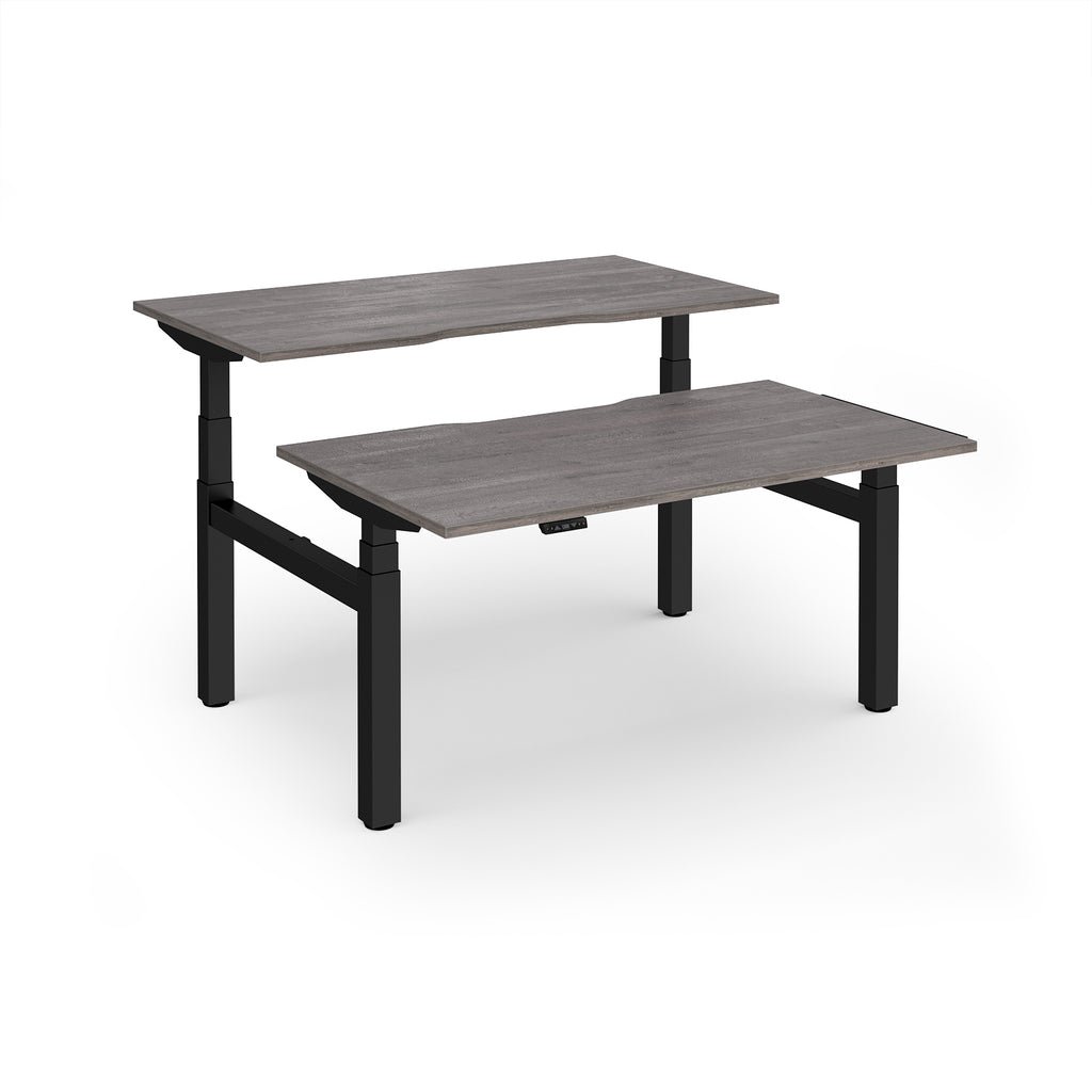 Two back-to-back height adjustable desks with shared black metal frame and grey wood-effect tops on a white background
