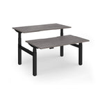 Two back-to-back height adjustable desks with shared black metal frame and grey wood-effect tops on a white background