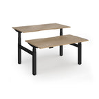 Two back-to-back height adjustable desks with shared black metal frame and wood-effect tops on a white background