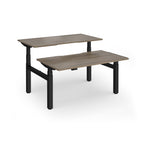Two back-to-back height adjustable desks with shared black metal frame and wood-effect tops on a white background
