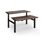 Two back-to-back height adjustable desks with shared black metal frame and wood-effect tops on a white background