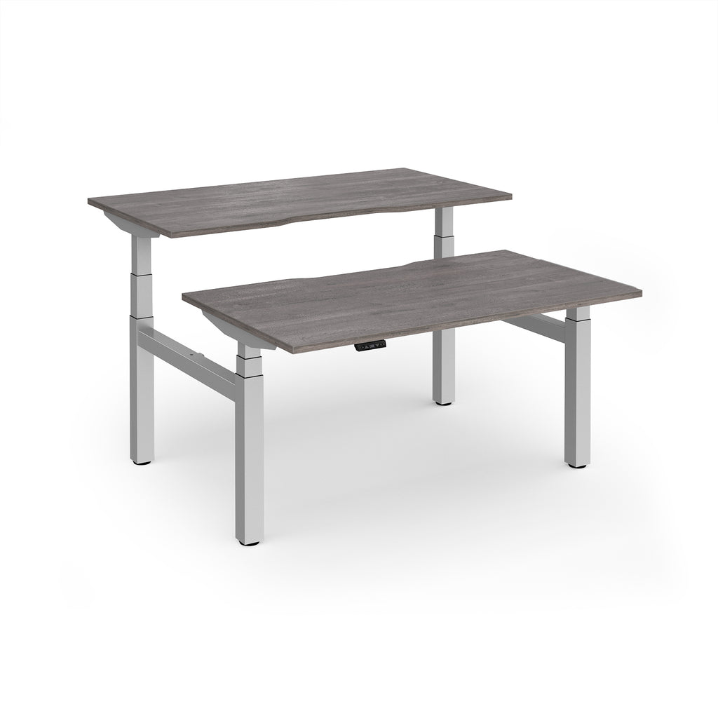 Two back-to-back height adjustable desks with shared silver metal frame and grey wood-effect tops on a white background