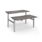Two back-to-back height adjustable desks with shared silver metal frame and grey wood-effect tops on a white background